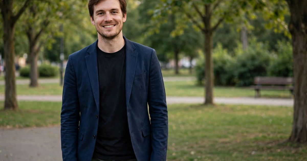 Illustration: AI-generated image of a fictional smiling European man in a navy blazer and black t-shirt standing alone in a park.